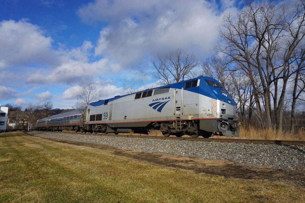 Silver and blue Amtrak passenger train with a diesel locomotive passing bare trees under a cloudy winter sky