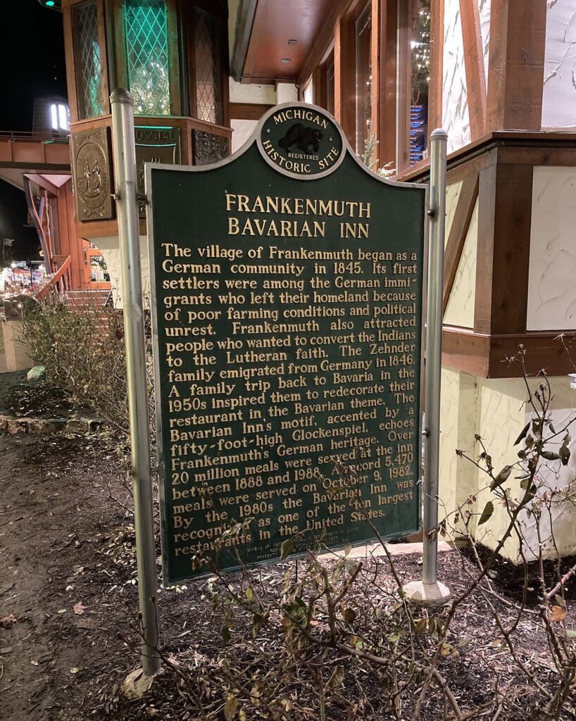 Green Michigan Historic Site marker for the Bavarian Inn, lit at night beside the restaurant's timbered wall