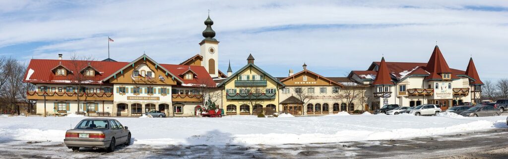 Wide view of the Bavarian Inn Restaurant, a long Bavarian-style building with red roofs and a central tower, in snow