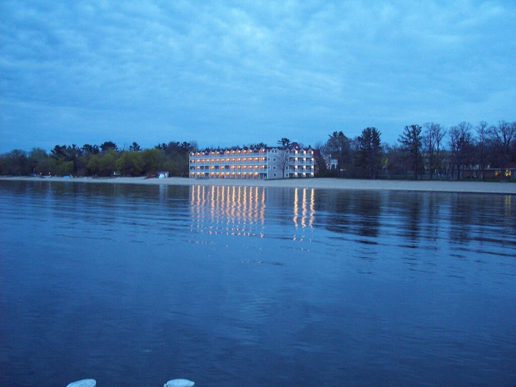 A four-story lakefront hotel lit up at dusk and reflected in the calm water of Grand Traverse Bay
