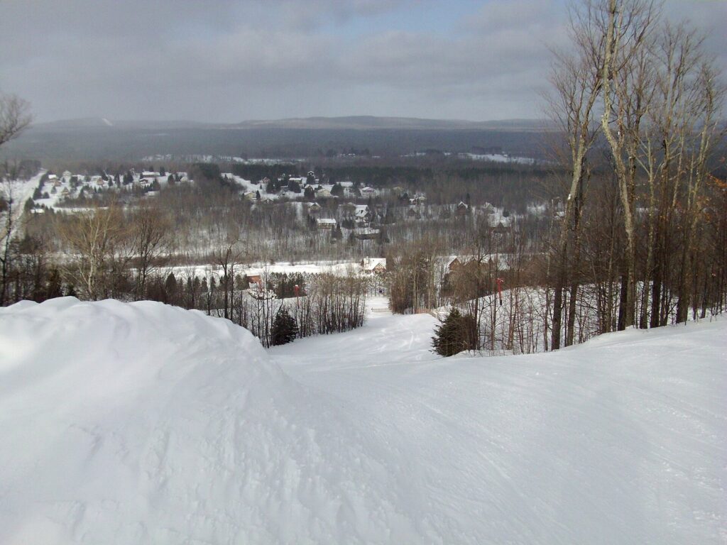View from a snowy ski trail at Big Powderhorn over a wooded valley and resort buildings