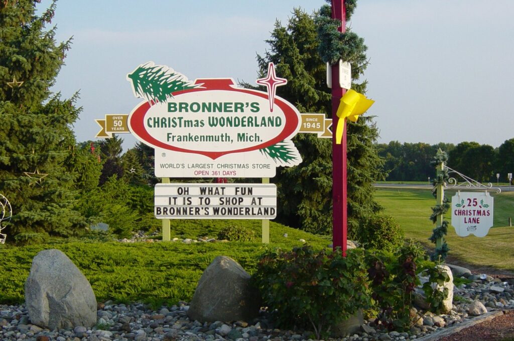 Roadside sign for Bronner's CHRISTmas Wonderland among evergreens, with Christmas Lane and open 361 days on the sign