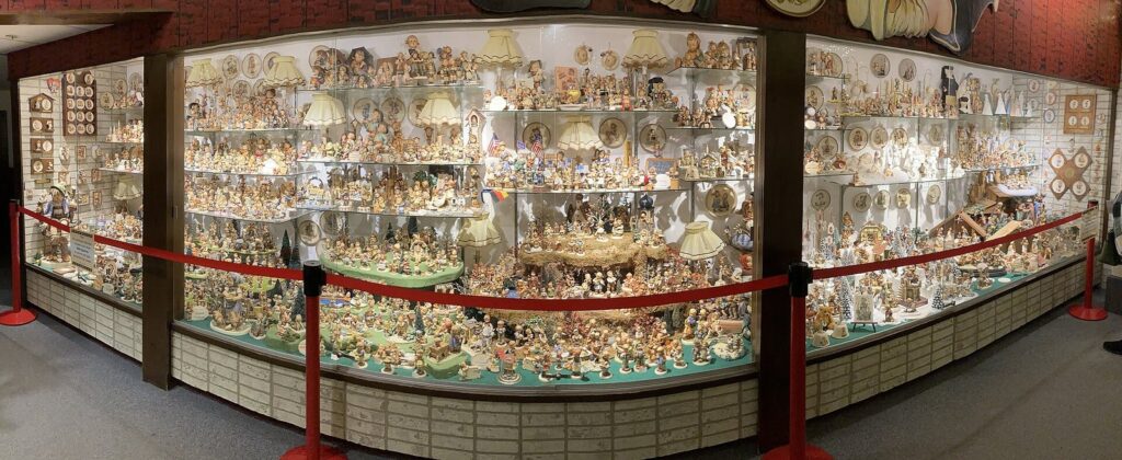 A long glass display case filled with rows of small porcelain figurines behind a red rope