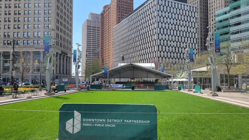 Green lawn with a white tent and trees in a square surrounded by downtown office towers