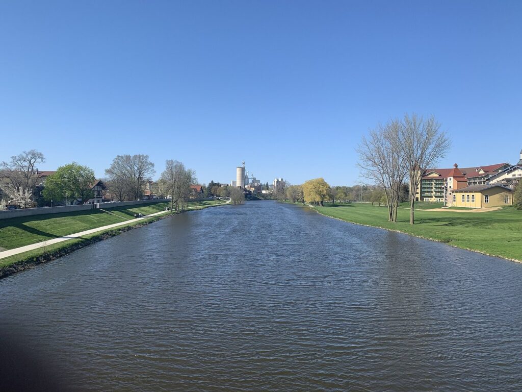 Calm river between grassy banks with a riverside path and a large chalet-style hotel on the right