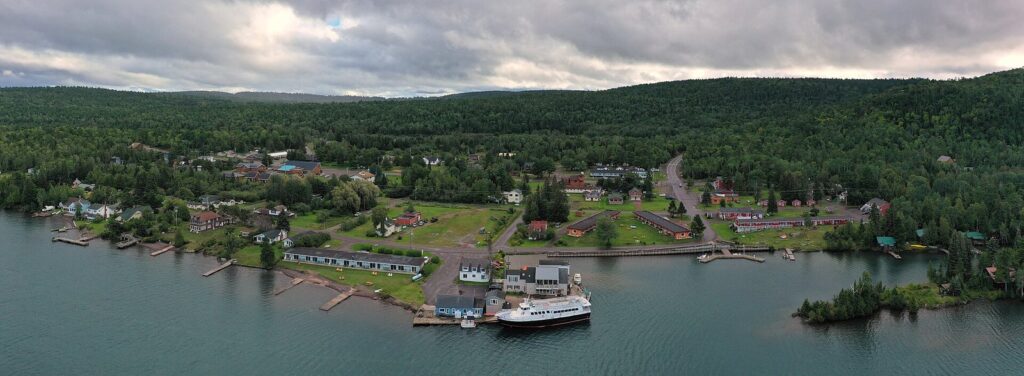 Aerial panorama of a small harbor town on a wooded shore with a ferry at the dock and Lake Superior around it