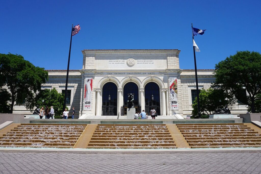 White marble facade of the Detroit Institute of Arts with three arched entrances, flags and stepped fountains