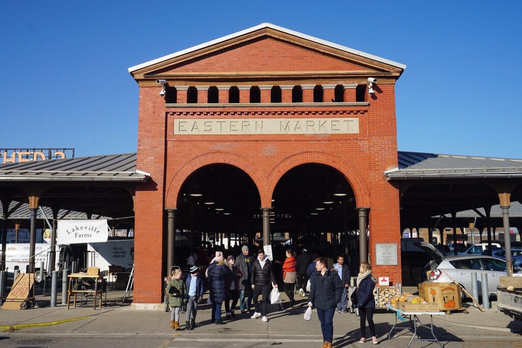 Red-brick Eastern Market shed entrance with arches and the market's name, with shoppers in front