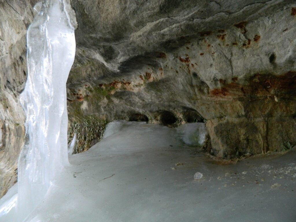 Column of ice hanging beside a sandstone overhang, with snow on the cave floor