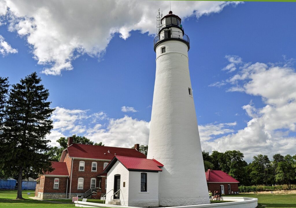 White conical tower of the Fort Gratiot Light with red-roofed keeper's buildings under a blue sky in Port Huron