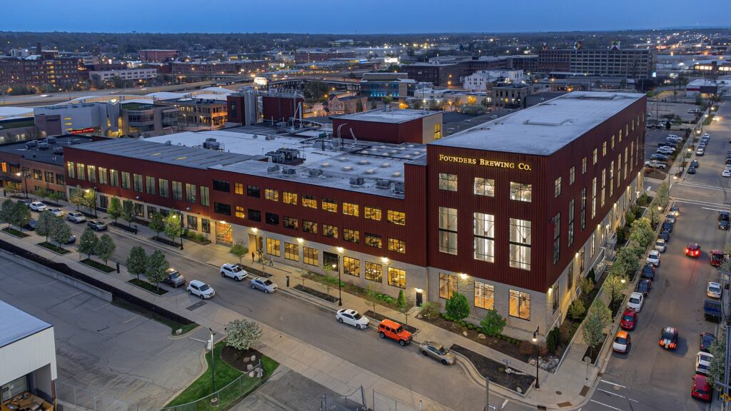 Aerial view at dusk of the large brick Founders Brewing Company building and its surrounding streets