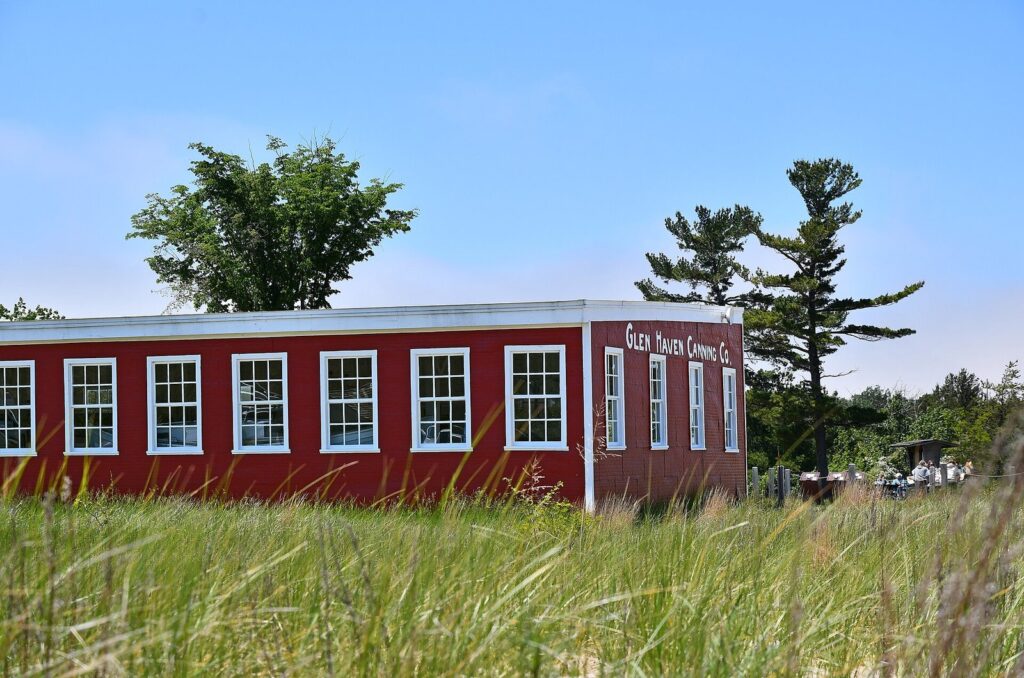 Red wooden Glen Haven Canning Co. building with white-trimmed windows behind tall beach grass