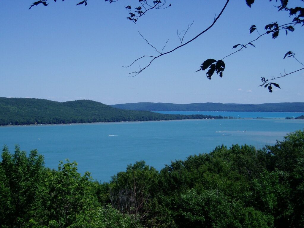Wide view of a clear blue lake between wooded hills, framed by leaves in the foreground
