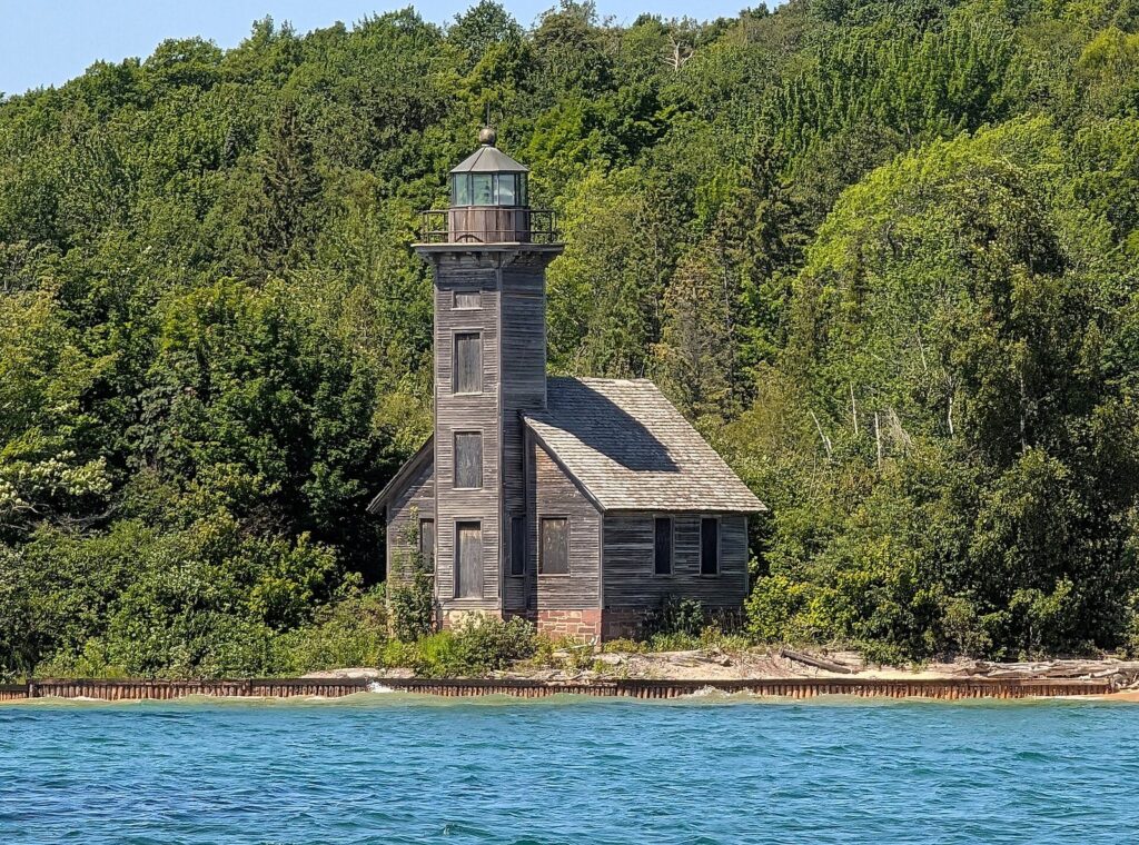 Weathered wooden lighthouse tower and keeper's house on a wooded shore above blue water