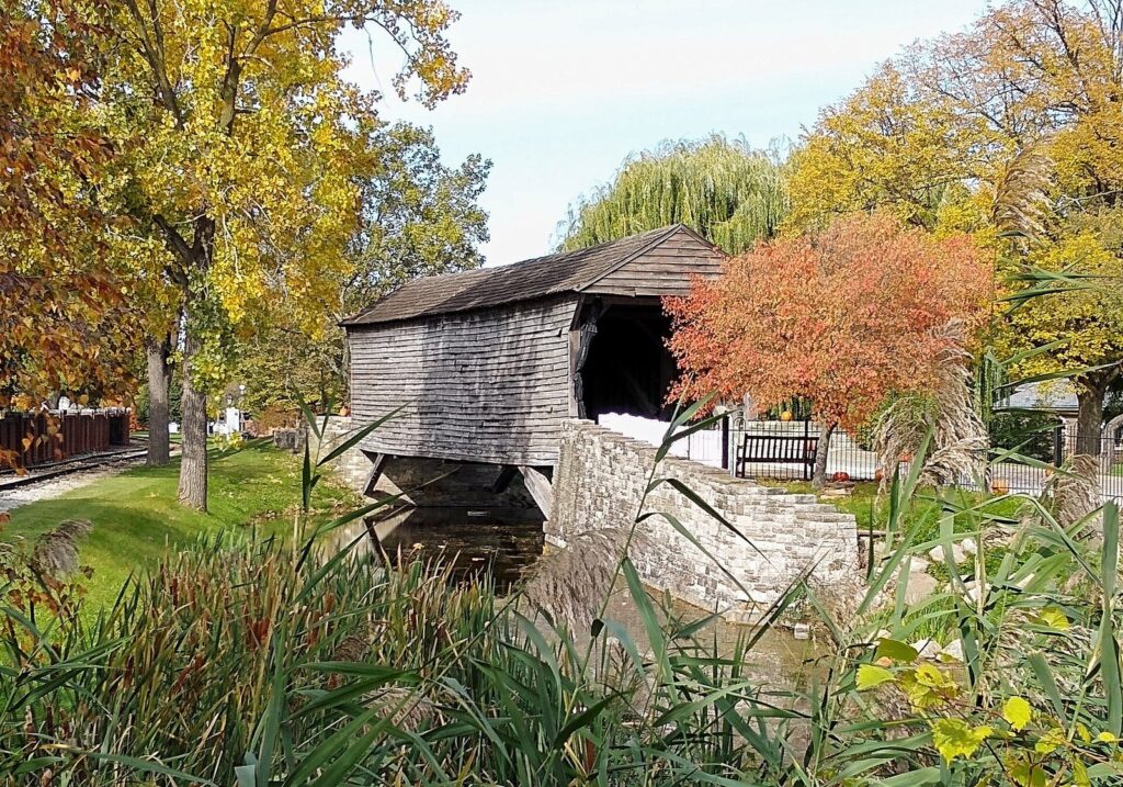 Weathered wooden covered bridge over a stream framed by autumn trees in orange and yellow