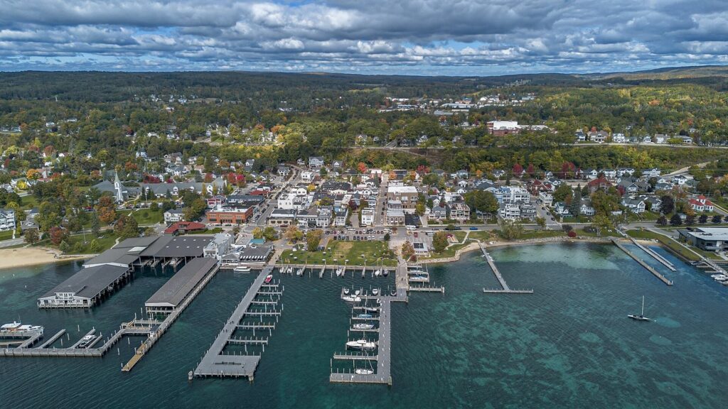 Aerial view of Harbor Springs, its marina and docks on clear green water, with the town and fall-colored hills behind