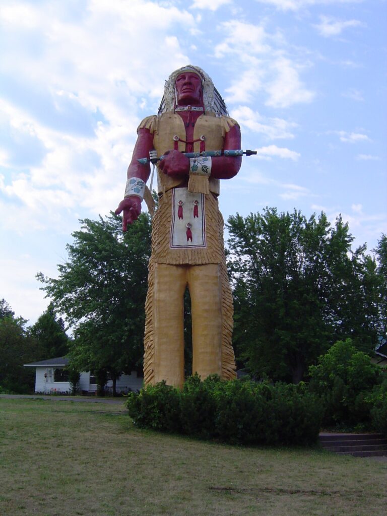 Giant painted statue of Hiawatha holding a pipe, standing above the trees in Ironwood