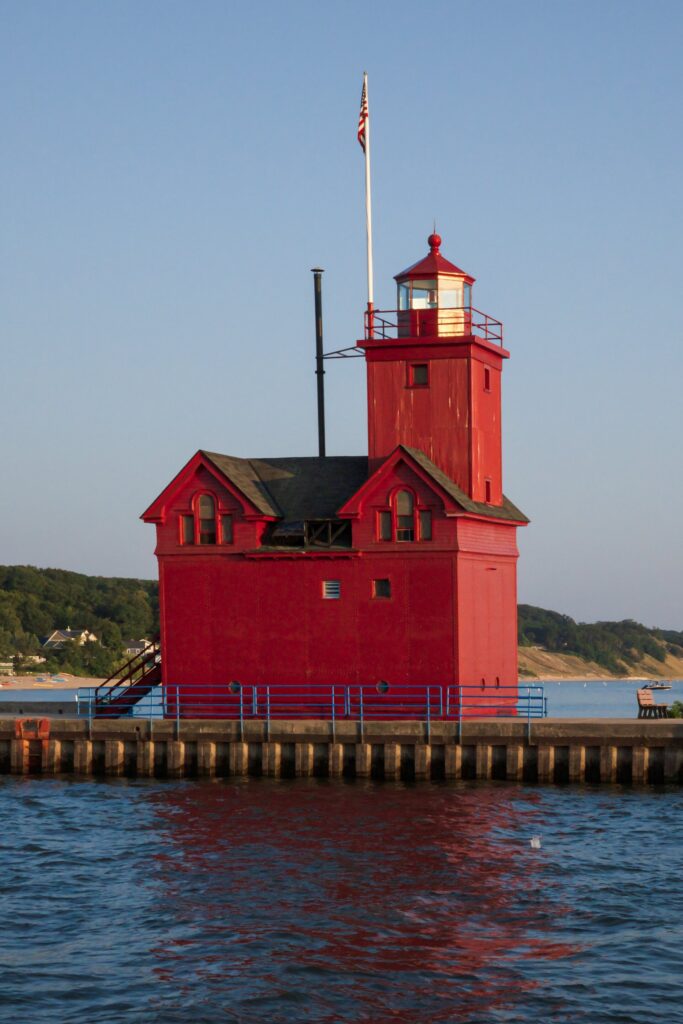 Bright red lighthouse with a gabled roof and square tower at the end of a pier over blue water