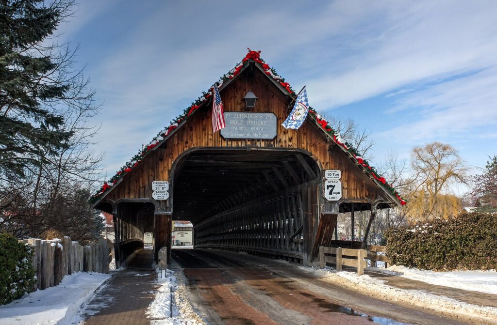 Entrance to a wooden covered bridge with a steep roof, holiday garlands and flags, in winter