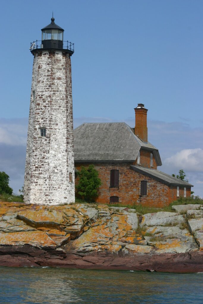 Tall stone lighthouse tower and brick keeper's house on a rocky islet of red rock above the water