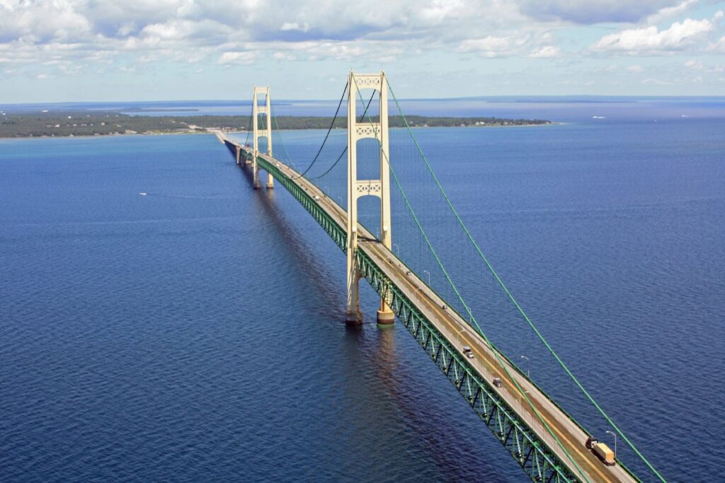 The Mackinac Bridge's ivory towers and green suspension span over deep blue water, seen from the air