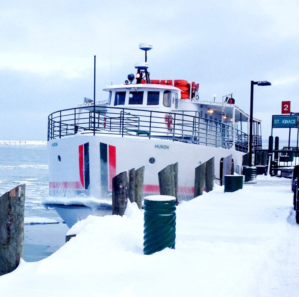 A white passenger ferry tied up at a snow-covered dock with ice on the water