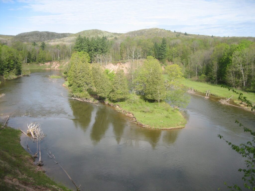 The Manistee River curving around a green island through a wooded valley with hills behind