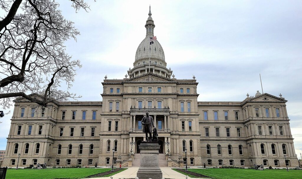 Michigan State Capitol in Lansing, a pale stone building with a tall white dome and a statue on the front lawn