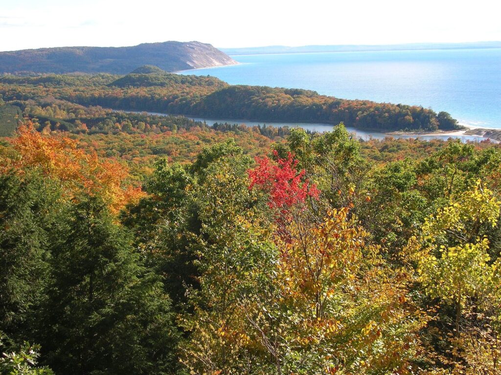 View over red, orange and green autumn forest to North Bar Lake, a sand spit and Lake Michigan