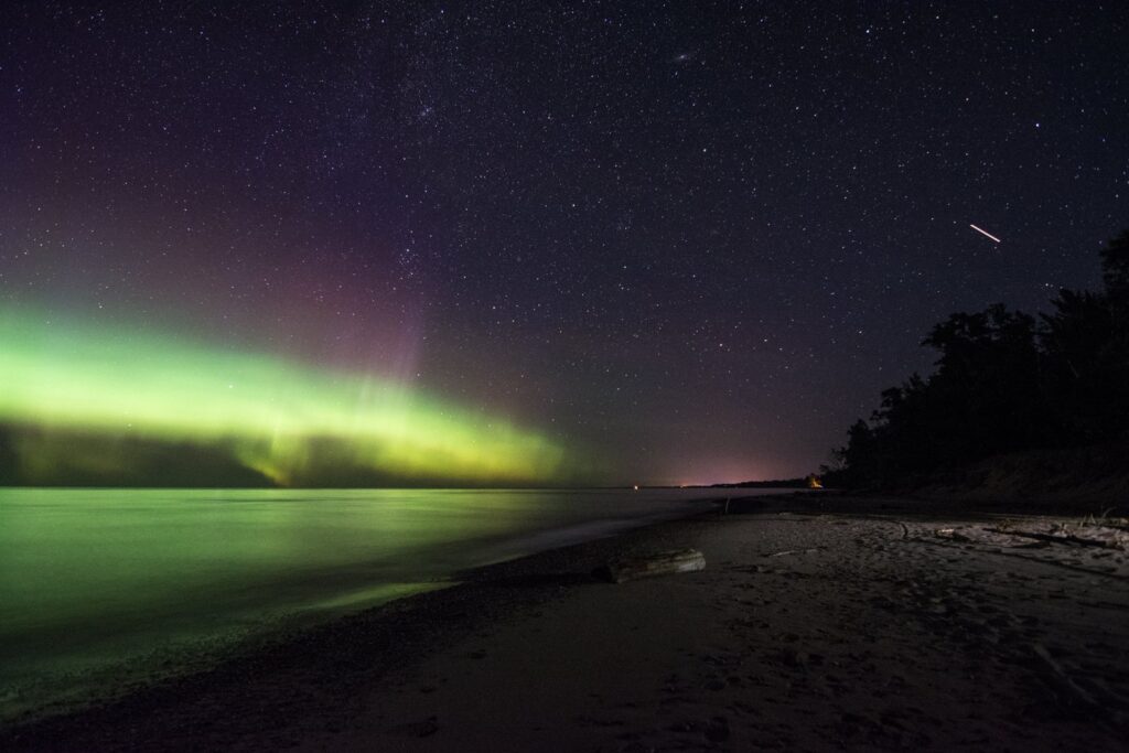 Green and purple northern lights over Lake Superior and a dark sand beach at Ontonagon