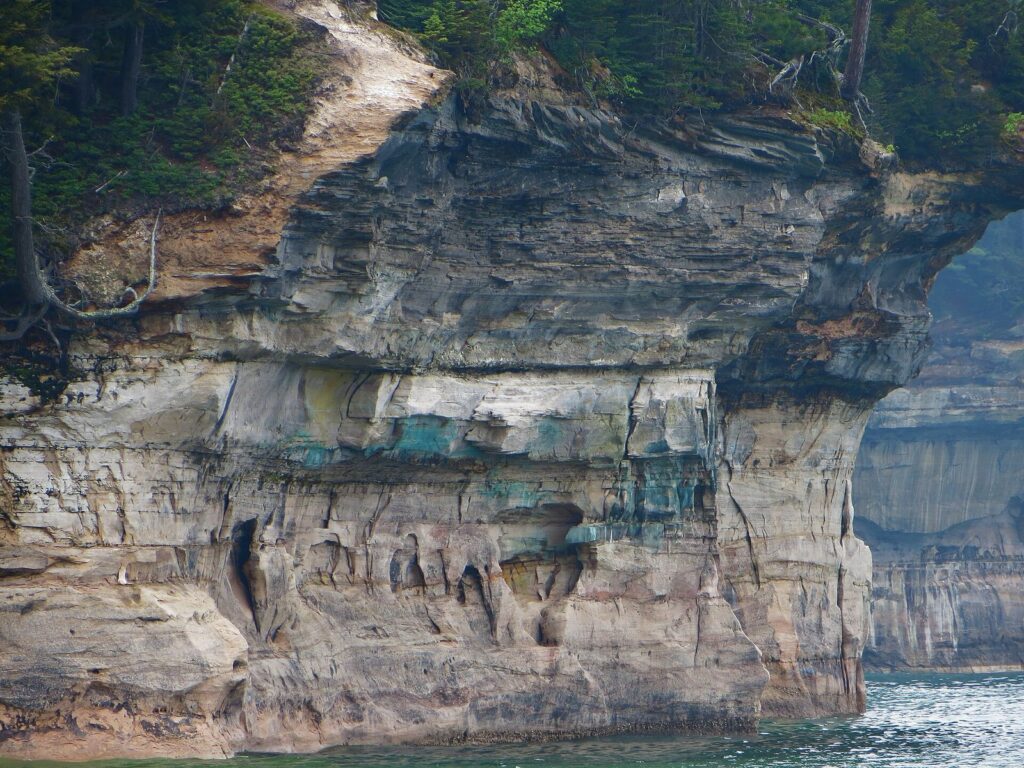 Close view of sandstone cliffs streaked with blue-green, orange and white mineral stains above breaking waves