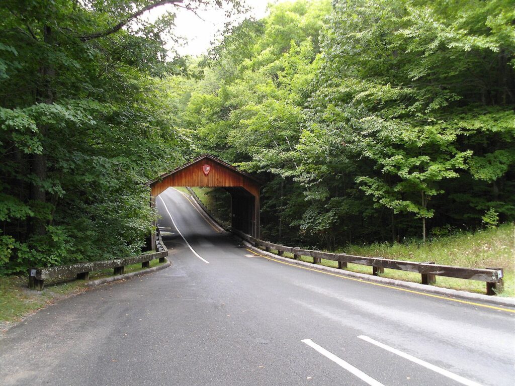 Red covered bridge over the paved scenic drive, surrounded by green summer forest
