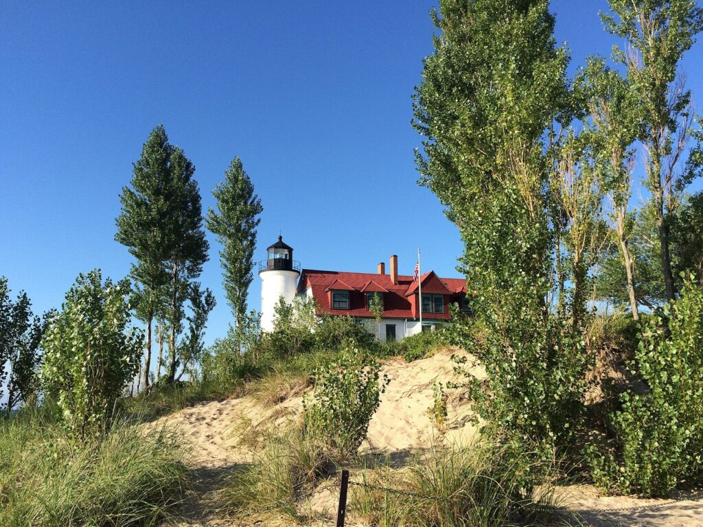 White lighthouse tower with a red-roofed keeper's house on a sandy dune among poplar trees