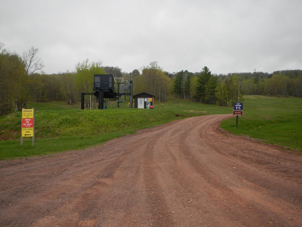 Chairlift terminal and grassy ski runs at the park's ski hill in spring, with forest behind