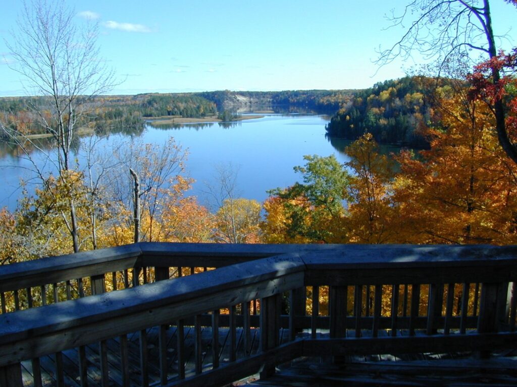 Wooden overlook deck above a wide blue stretch of the Au Sable River with orange trees on the bank