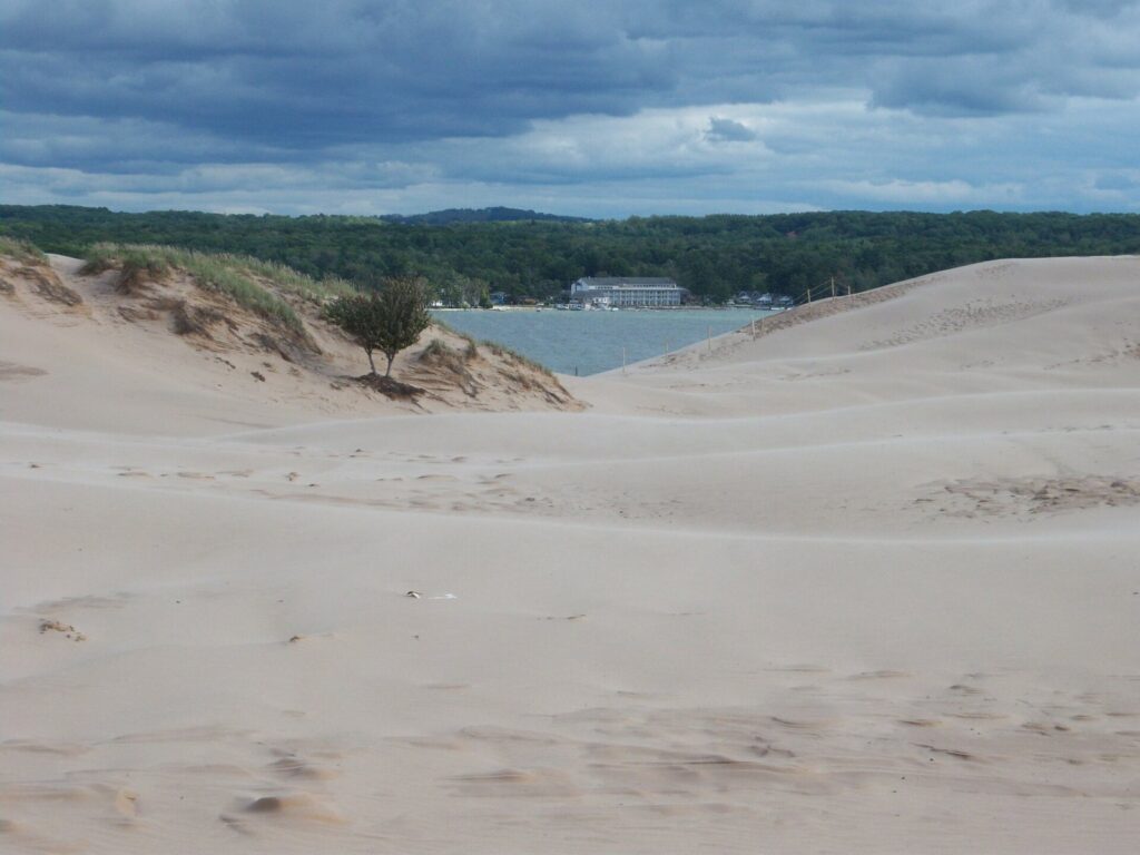 Open sand dunes rolling down toward Silver Lake, with forest and a distant shoreline under a cloudy sky