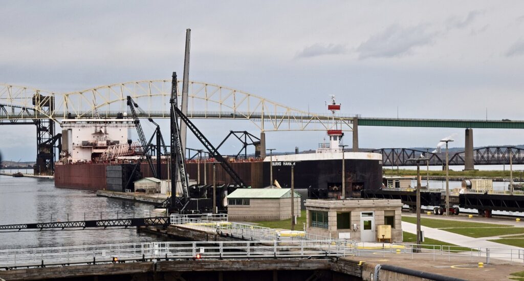 A large freighter entering a lock at the Soo Locks, with the arched International Bridge behind