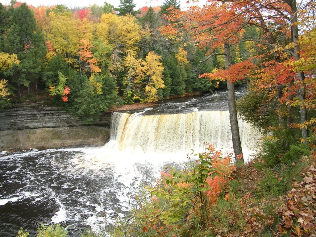 Upper Tahquamenon Falls with amber water and orange, yellow and green trees on the far bank