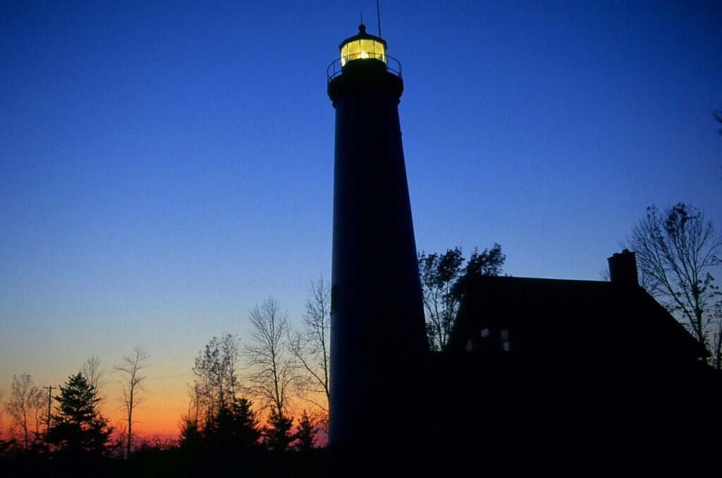 Tawas Point Lighthouse and keeper's house in silhouette against an orange and blue twilight sky