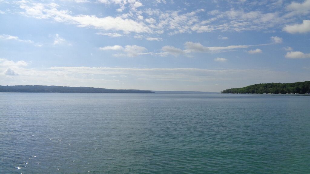 Clear blue-green water of Torch Lake with wooded shores under a summer sky