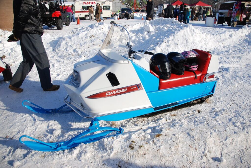 Vintage blue-and-white snowmobile parked in the snow at a winter festival with food stands behind