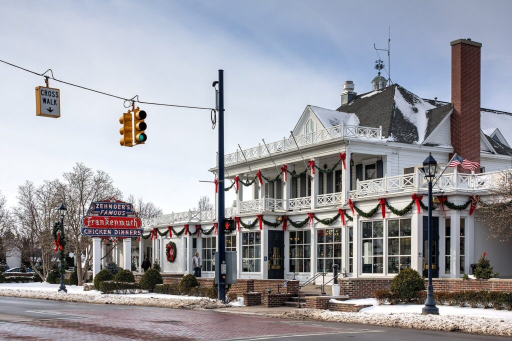 White colonial-style Zehnder's restaurant with a two-story porch, holiday garlands and a neon chicken dinner sign